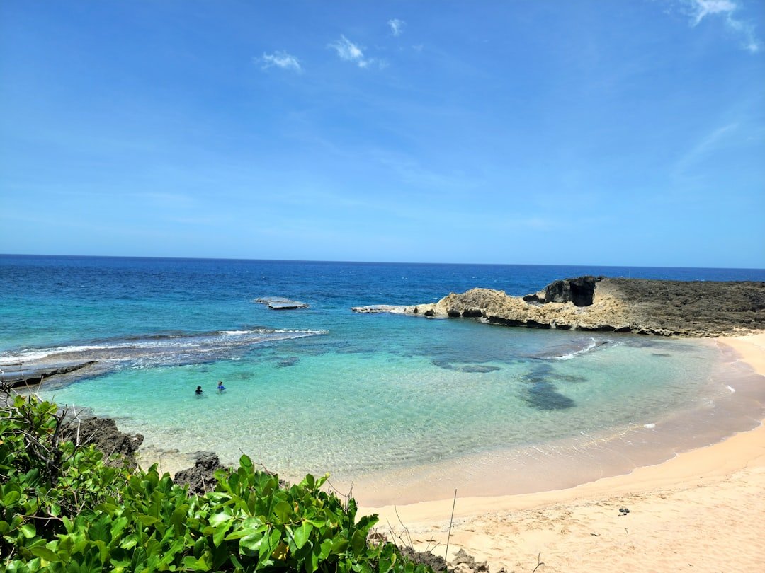 a sandy beach with clear blue water and a rock outcropping
